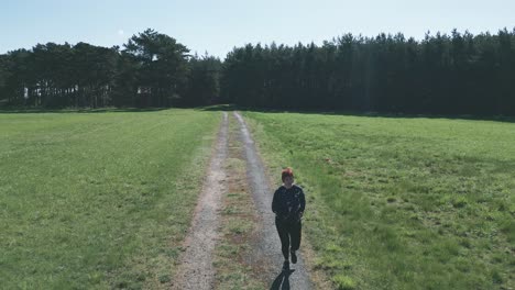 Wide-shot-of-a-woman-running-down-a-dirt-road-from-the-woods-in-running-clothes