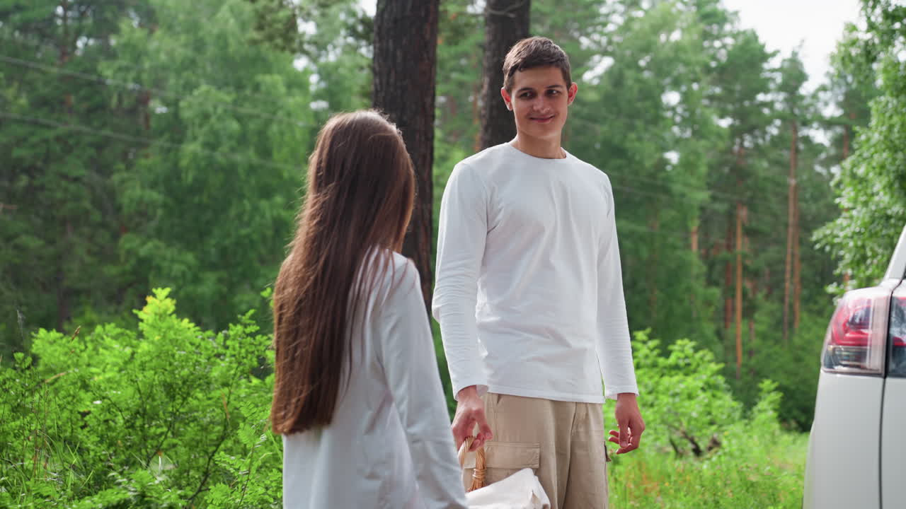 밝은 초록색 숲으로 둘러싸인 곳에서 오빠가 여동생에게 즐거운 미소로 피크닉 바구니를 건네고 있어요. 야외 피크닉을 준비하는 가족의 모습은 사랑, 유대감, 그리고 연결을 보여주는 자연스러운 여름날의 한 장면이에요.