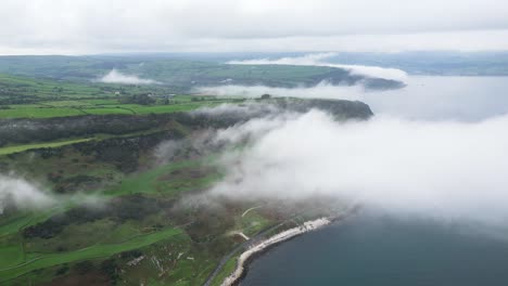 Toma-Aérea-De-La-Hermosa-Naturaleza-De-Irlanda-Del-Norte-Con-Vista-A-La-Carretera-Costera-Cerca-De-La-Ciudad-De-Glenarm,-Rocas-Naturales-Y-El-Mar-Azul-Tranquilo-Sobre-Las-Nubes