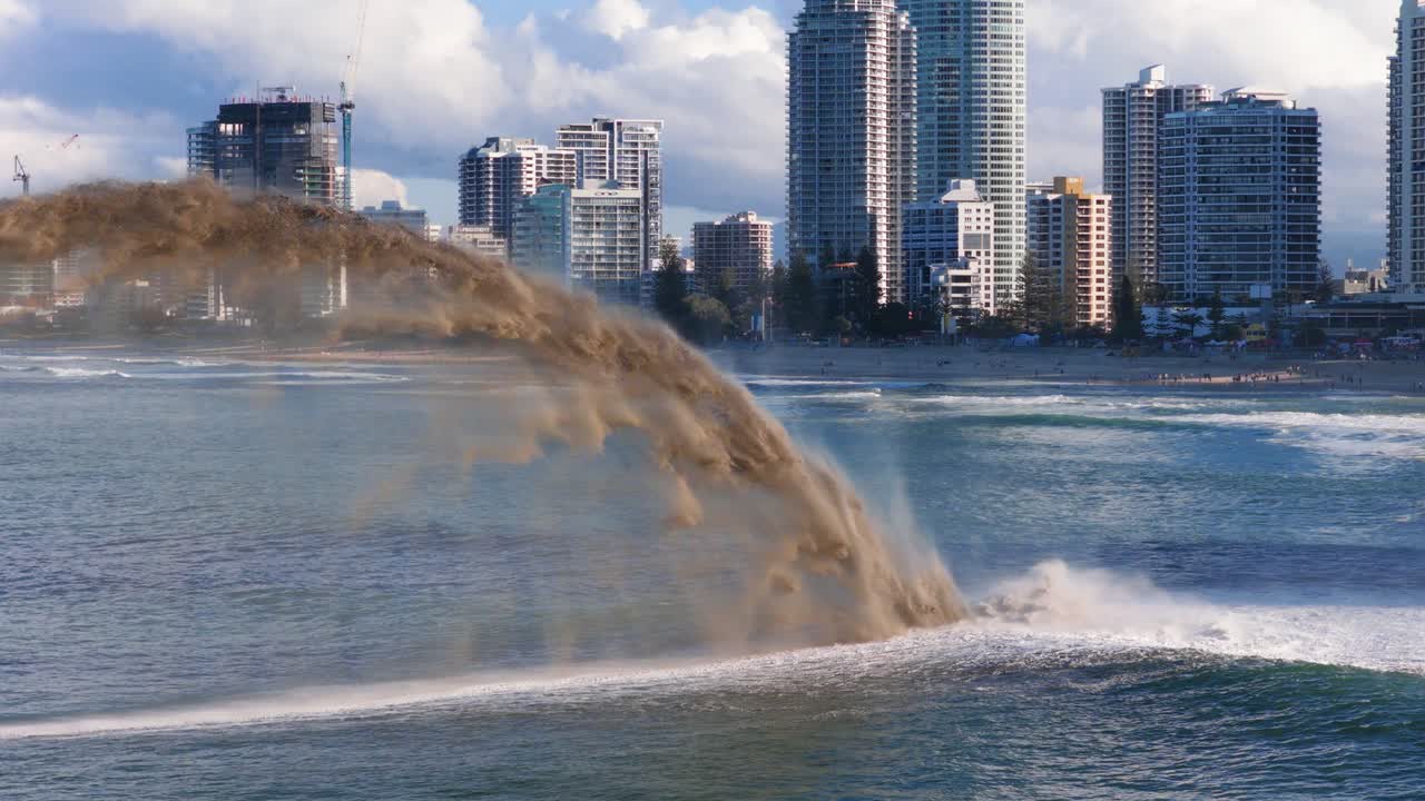 A boat sprays sand over water against a city skyline under bright daylight