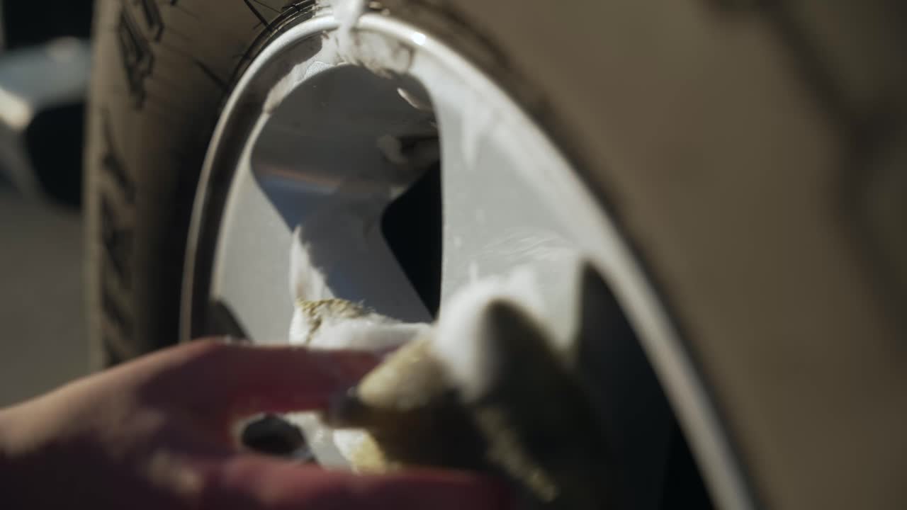 Close-up hand scrubbing soapy water on SUV rim in bright daylight