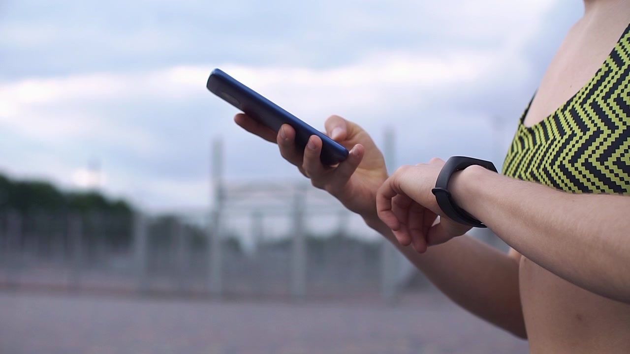 Woman Checking Fitness Tracker and Smartphone Outdoors