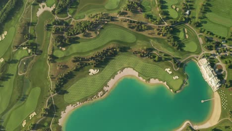 Aerial-reveal-shot-of-a-golf-resort-with-beautiful-abstract-patterns,-sand-traps,-trees,-and-a-turquoise-lake