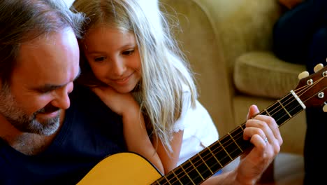 father playing guitar with her daughter in living room 4k