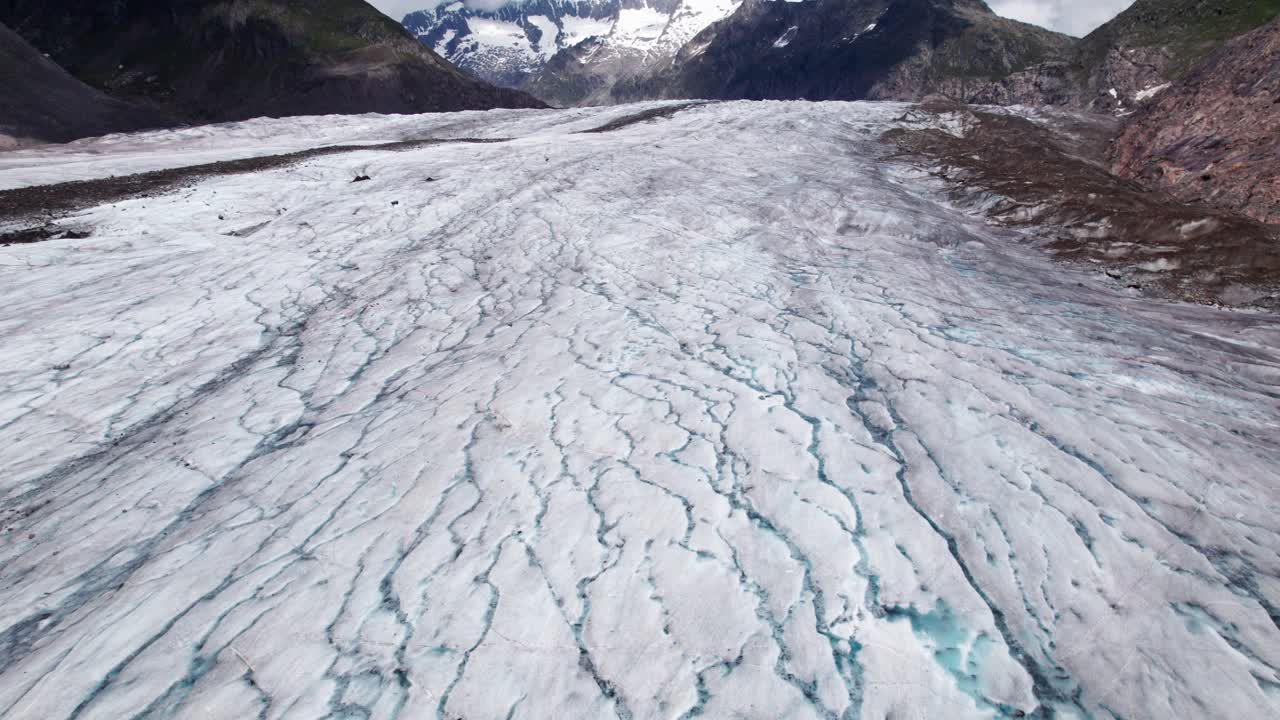4K drone flight over the vast Aletsch Glacier, showcasing textured ice, sweeping alpine valleys, and towering Swiss mountain peaks in a dramatic high‑altitude landscape