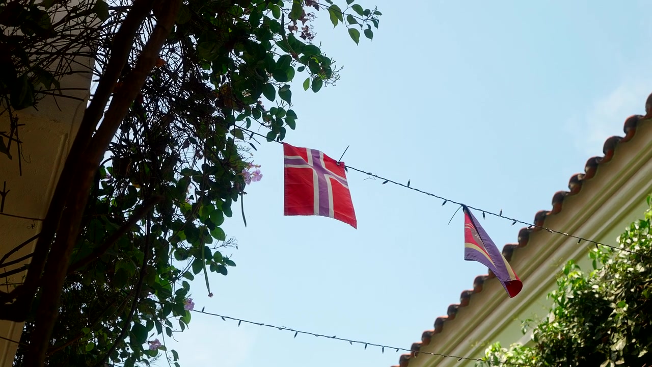 Norsk flag hængende over en gårdhave i kolonistil med omkringliggende arkitektur og klar blå himmel. Filmet i Cartagena de Indias, Colombia, Sydamerika.