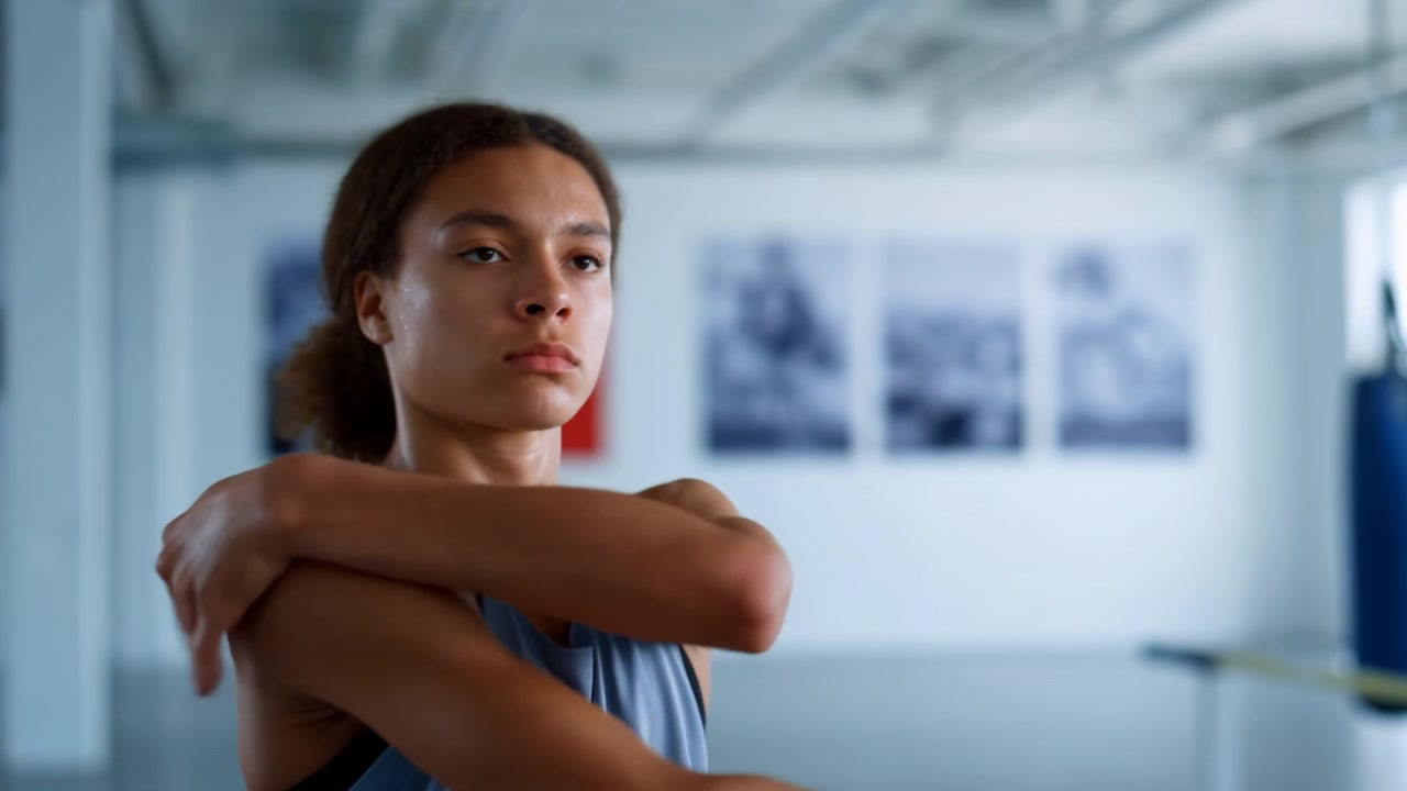 Close-up view of young female athlete holding standing stretch poses in indoor gym, with upper torso, shoulders, and face in tight crop, showing focused warmup movement and calm determination