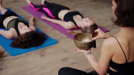 mujer usando cuencos de canto durante la meditación, dirigiendo una clase de yoga al aire libre