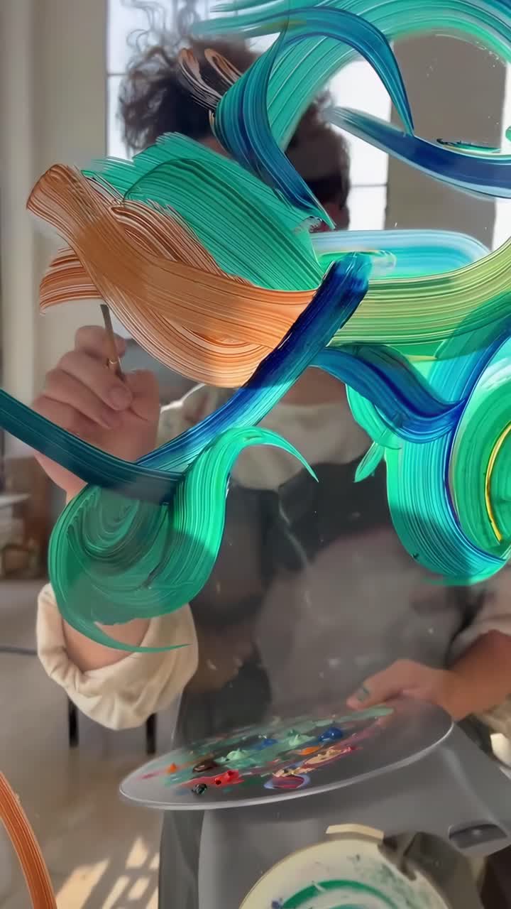 Close-up video of an artist painting on glass, vibrant brushstrokes, dynamic angle