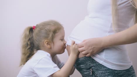 una niña linda besa el abdomen de su madre embarazada en una habitación luminosa