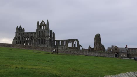 une photo lentement panoramique montrant une femme poussant une poussette à l'abbaye de whitby pendant la journée.