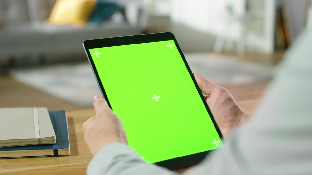 hombre usando pantalla de maqueta verde computadora tableta digital en modo retrato mientras está sentado en su escritorio. en el fondo acogedora sala de estar.