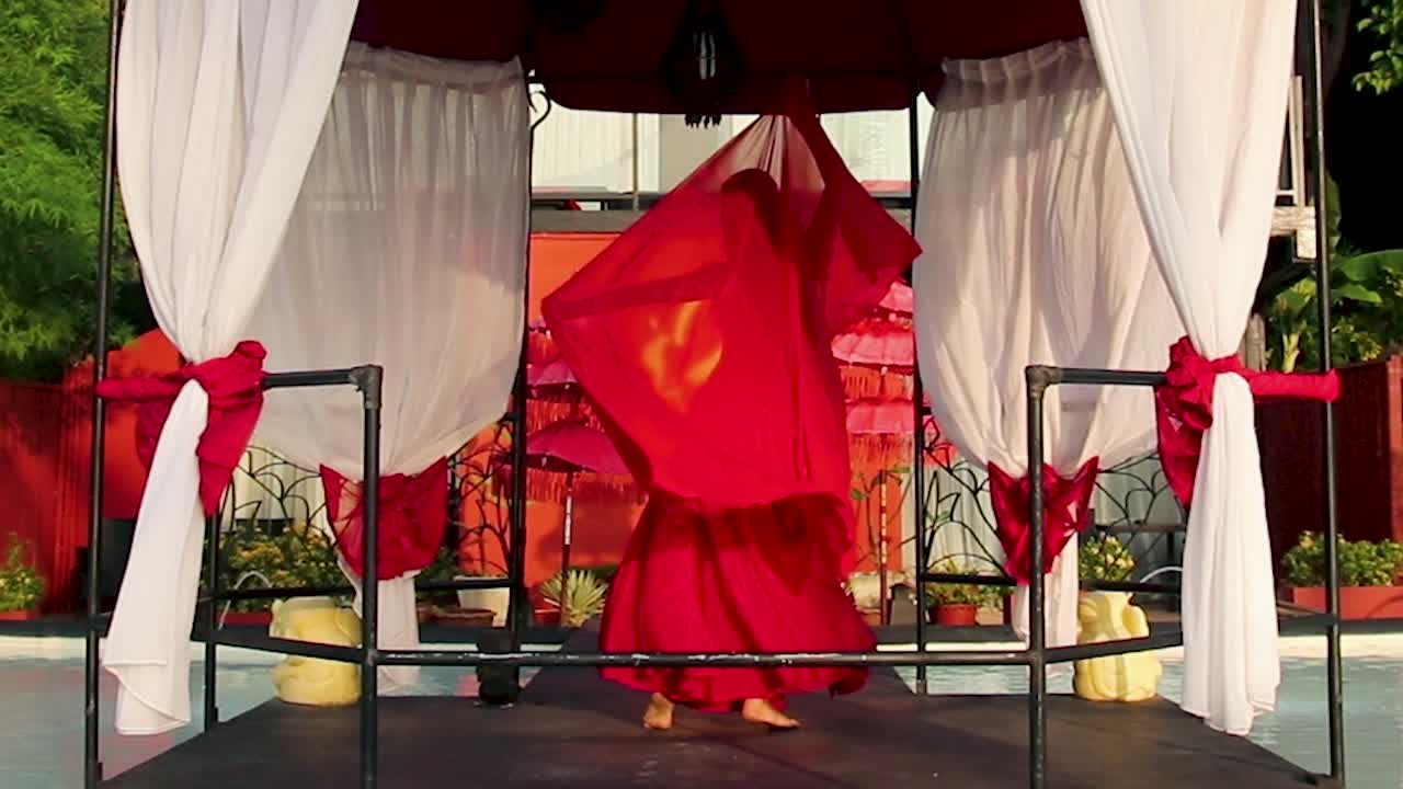 Hot, elegant, young and sexy belly dancer in red dress, performing under an Arabian gazebo