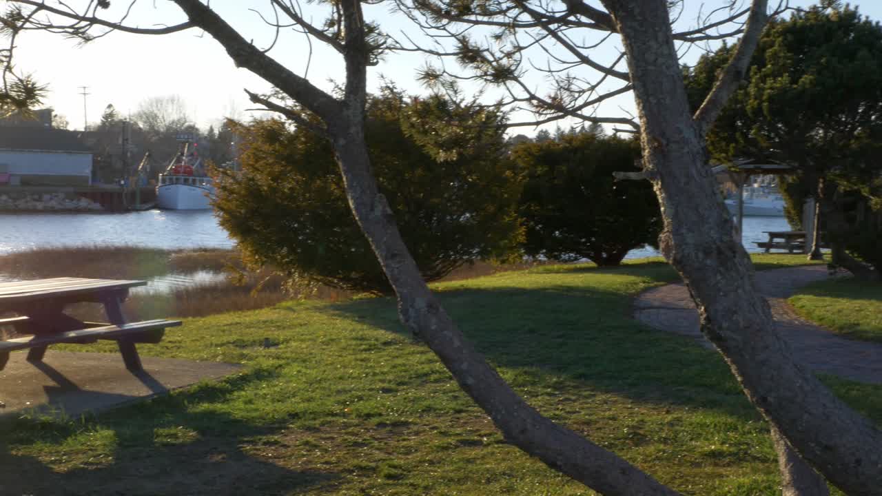 A panning shot of a park that sites on the sea. The sun is setting, causing a beautiful lens flare as the camera moves to reveal a gazebo.