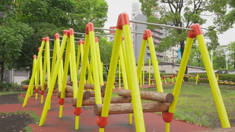 a close-up, low-angle shot of a bright yellow and orange jungle gym on an overcast day. a park with trees and buildings are in the background