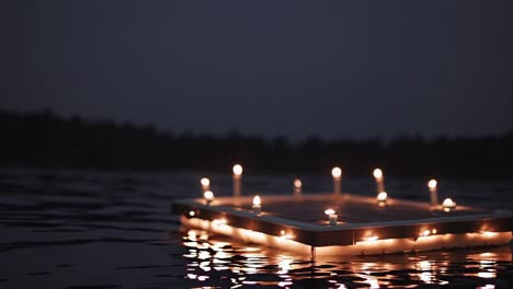 several lit candles casting a warm glow illuminate a small wooden dock, floating gently on a calm lake at dusk, evoking a tranquil and peaceful atmosphere perfect for relaxation