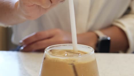 hand stirring iced coffee with a straw