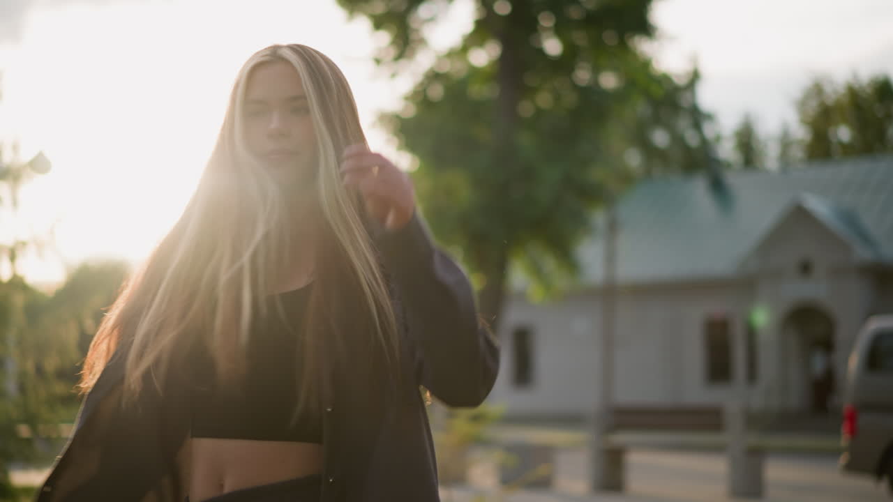 леди с радостью поворачивает по часовой стрелке в травяном поле, как она тянет волосы назад, солнечный свет создает сияющую атмосферу вокруг нее, фон включает в себя зелень, деревья и здание