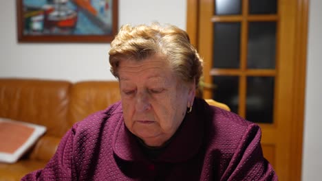 Elderly-woman-alone-in-a-purple-robe-sitting-in-a-room-with-warm-lighting