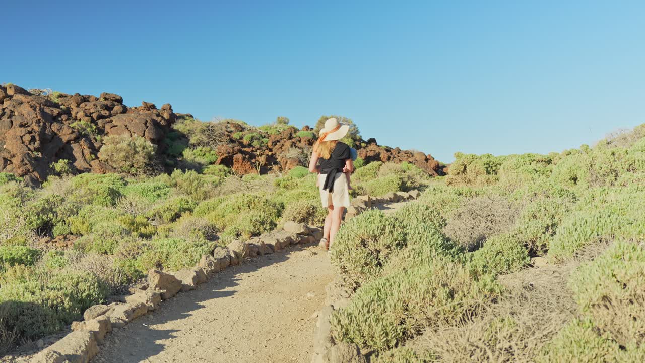 mujer con bebé caminando en el parque nacional del teide, vista trasera