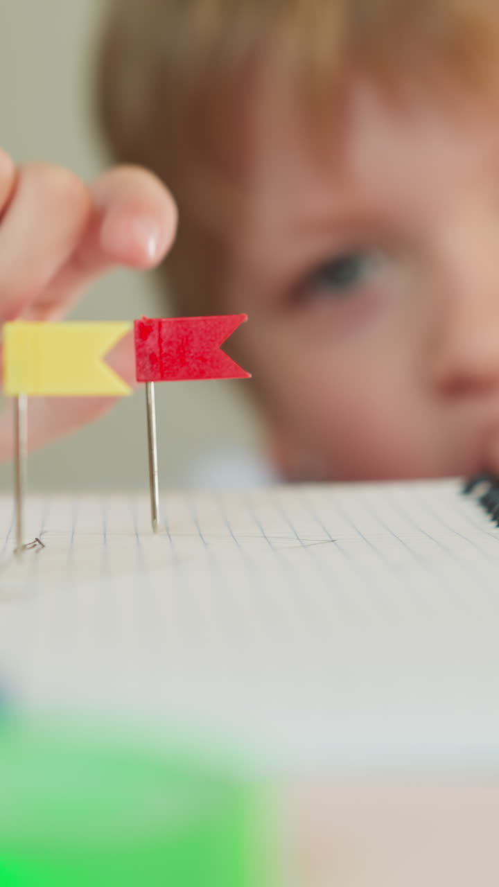 niño pequeño alcanza una pequeña bandera roja en el alfiler con los dedos en la mesa en el primer plano de la clase de jardín de infantes. niño pequeño lúdico y etiquetas de ubicación en el cuaderno en la lección