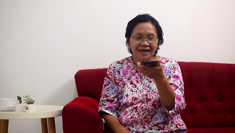 modern elderly asian woman talk on cell phone using loudspeaker at home