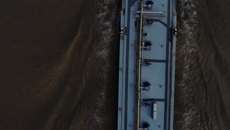 heavy loaded blue tanker sailing foreward on a dark colored river using it navigating radar. drone dolly shot from above.