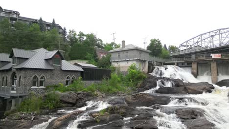still shot of the small waterfalls in the muskoka district in ontario, canada with cloudy skies and some old buildings