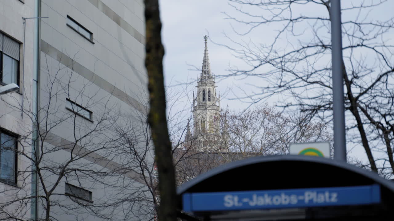 A striking Gothic tower rises behind the modern structures surrounding St.-Jakobs-Platz in Munich, Germany. The juxtaposition of historical and contemporary architecture