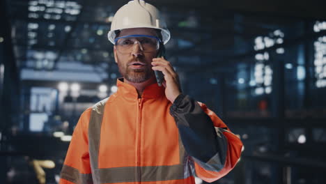 artesano profesional hablando por teléfono móvil en el almacén de la fábrica en uniforme de primer plano
