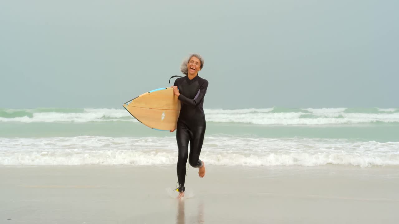 해변 4k에서 서핑 보드와 함께 활동적인 시니어 아프리카계 미국인 여성 서퍼의 앞면