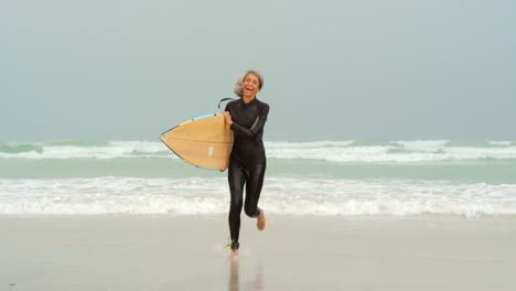 front view of active senior african american female surfer with surfboard running on the beach 4k