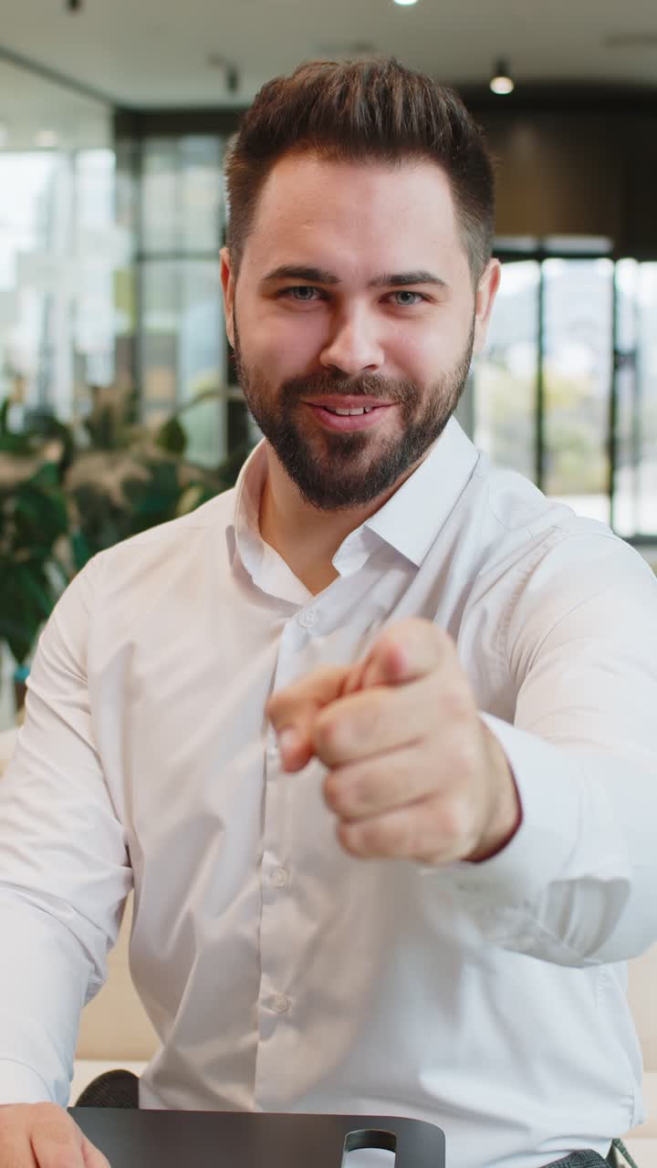 Ritratto di un giovane uomo d'affari caucasico che indica la fotocamera, scegliendo chi assumere, seduto nella hall dell'ufficio.