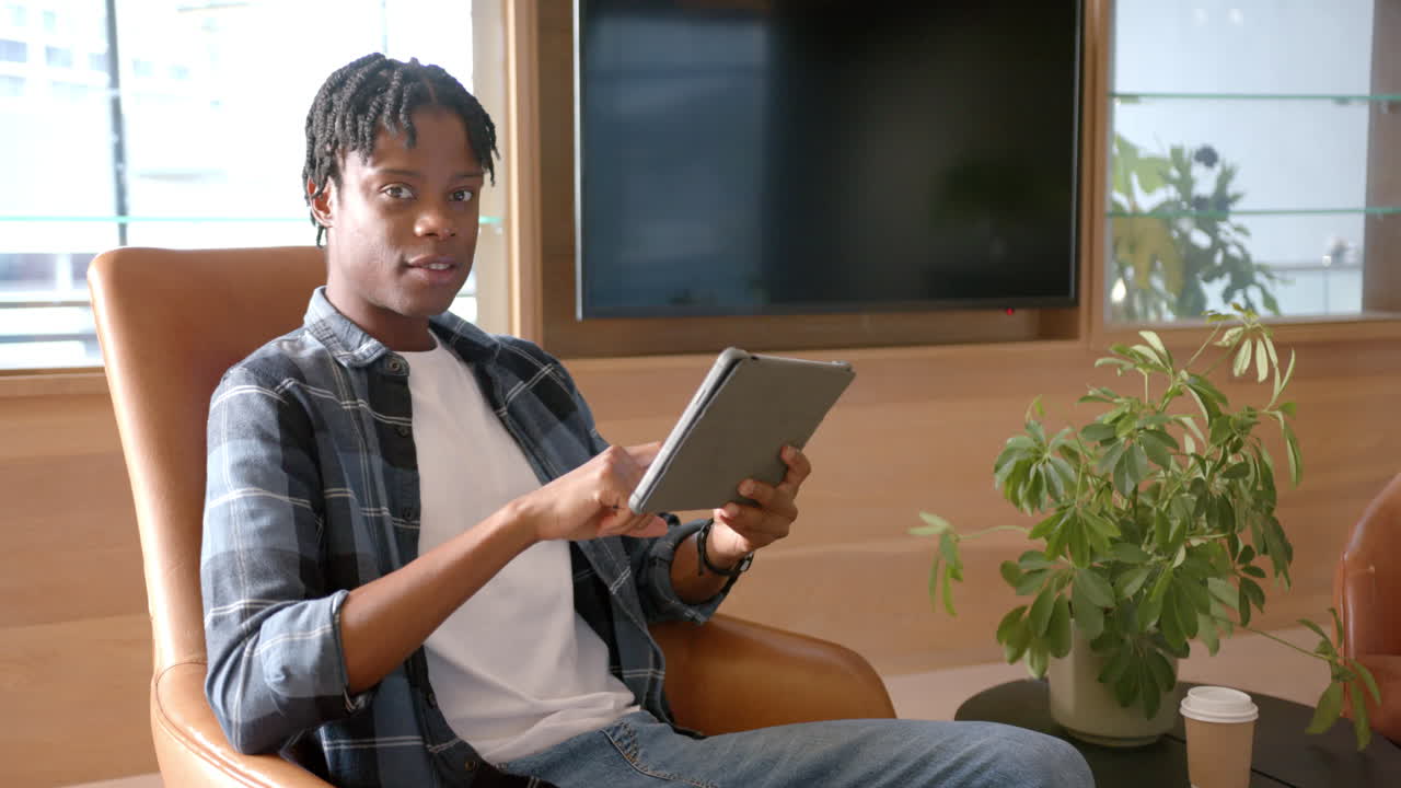Using tablet, man sitting in chair and working in modern office setting