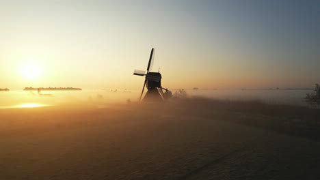 Drohnenschuss,-Der-Sich-Links-Von-Einer-Holländischen-Windmühle-Dreht,-Mit-Einem-Nebligen-Morgensonnenaufgang-Im-Hintergrund-In-4k