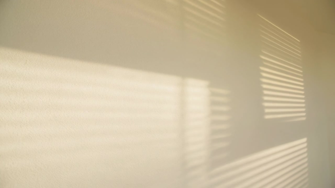 Sunlight through window blinds moves across pale cream interior wall, producing layered horizontal shadows that shift gently while bright light bands expand and soften inside quiet minimalist room