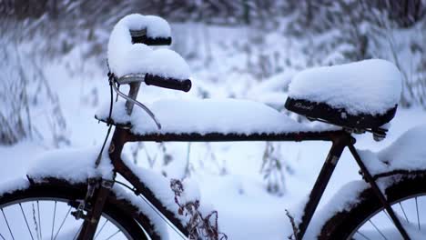 a bicycle sits quietly in a snow-covered landscape, its seat and handlebars blanketed with snow. the serene surroundings evoke a peaceful winter atmosphere in a secluded area.