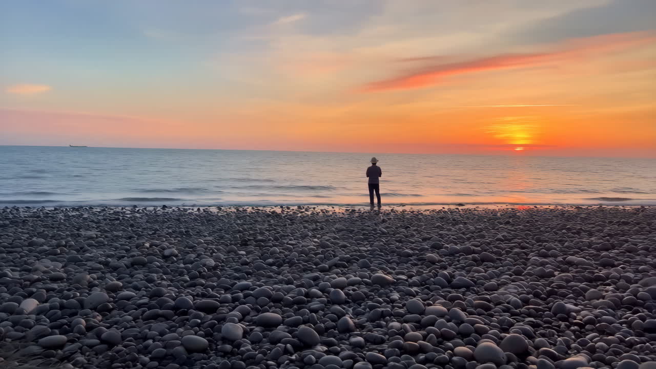 Person, der står på en stenstrand og ser en smuk solnedgang over havet