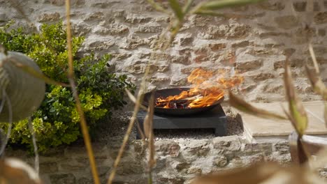 flames rage from small firewood in black traditional ceremonial bowl urn on pedestal