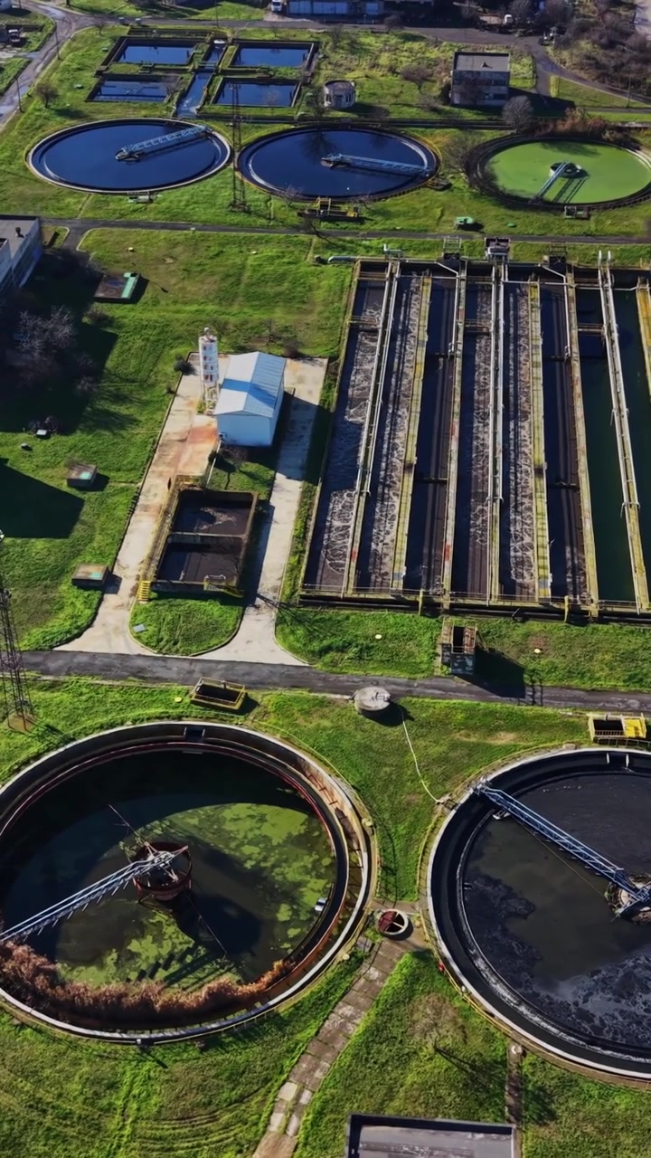 Water treatment facility with large tanks and greenery in daytime