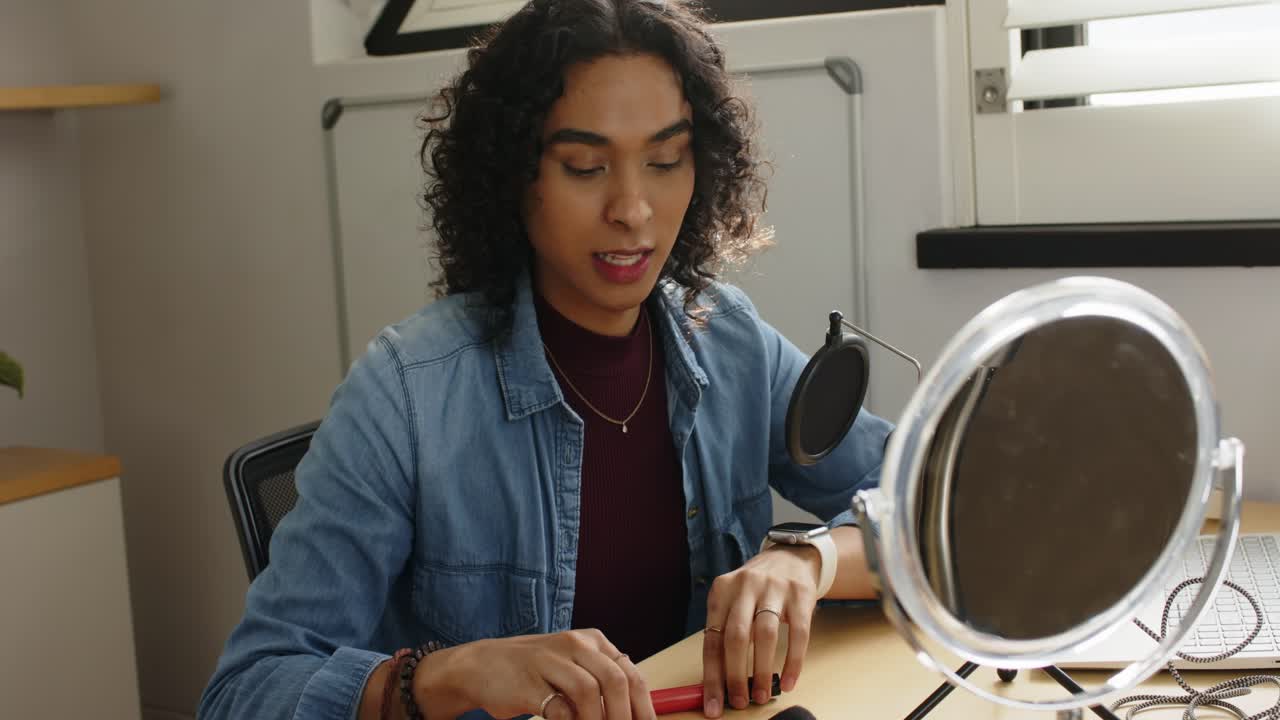 Non-binary creator showing red lip gloss shade before demoing powder brush usage tip at home studio