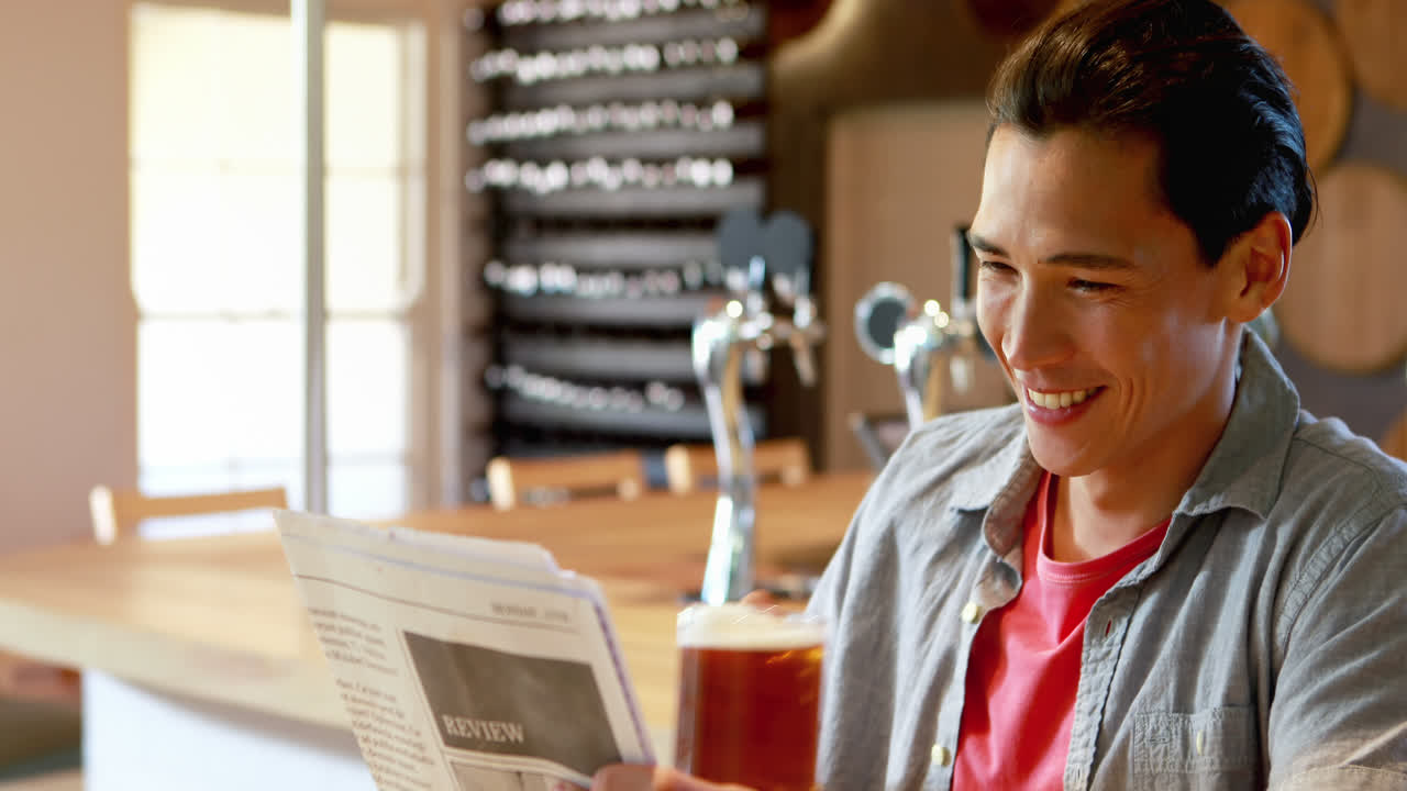 hombre tomando cerveza mientras lee el periódico en un restaurante 4k