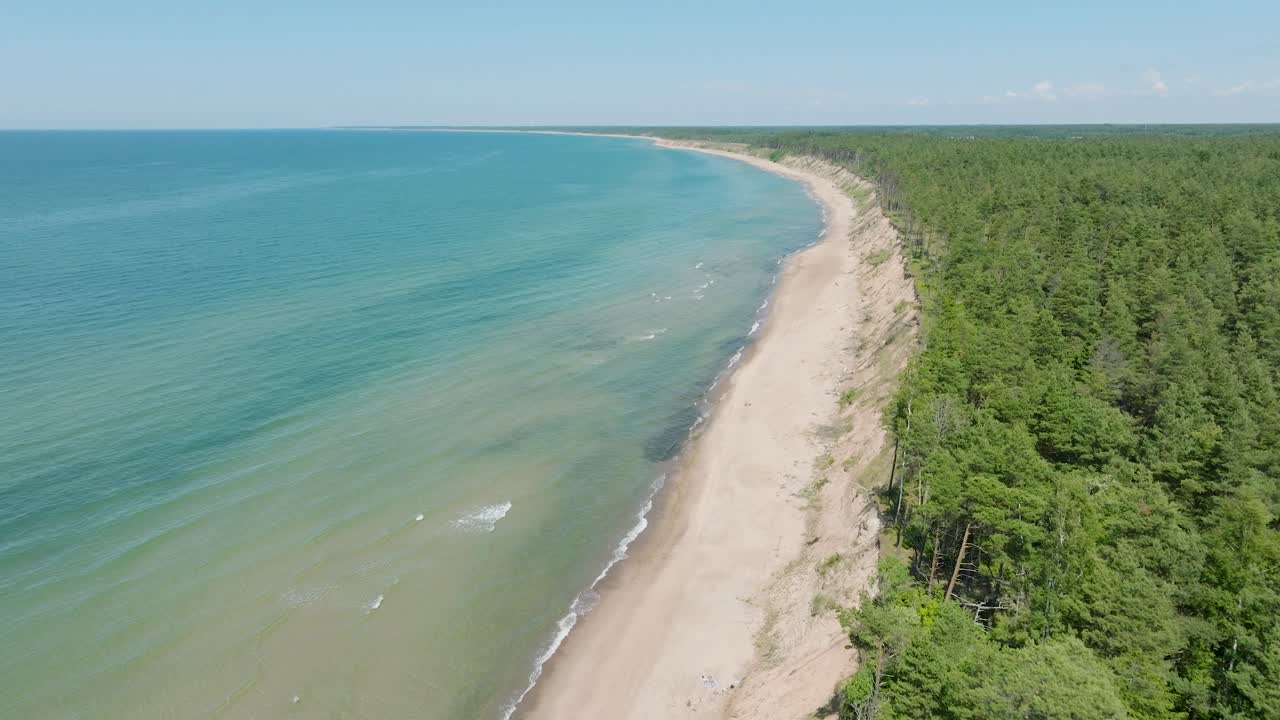 Aerial establishing view of Baltic sea beach at Jurkalne on a sunny summer day, white sand cliff damaged by waves, coastal erosion, climate changes, wide drone shot moving backward