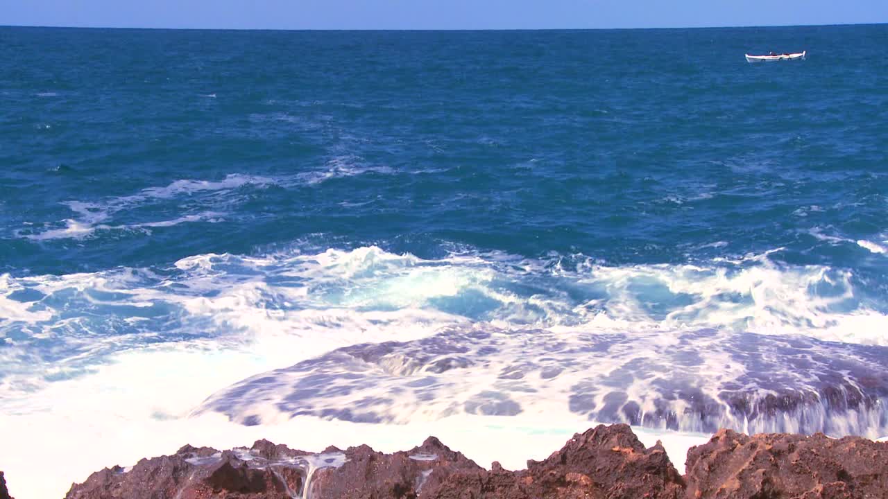 멀리 떨어진 작은 어선과 함께 해안선에 부서지는 파도의 넓은 샷 1