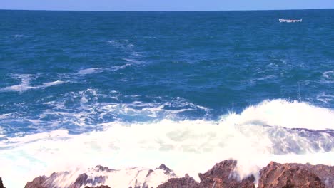 toma amplia de olas rompiendo en la costa con un pequeño barco de pesca distante 1