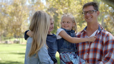 parents carrying their two young kids in park look to camera