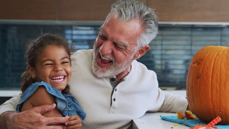 Portrait-Of-Grandfather-And-Granddaughter-Carving-Halloween-Lantern-From-Pumpkin-At-Home