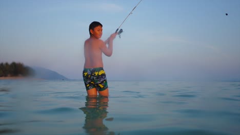 boy fishing in the sea at sunset
