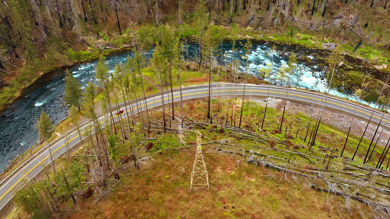 Narrow river going around the mountain with scarce vegetation. Red car moves by the highway at the foot of the rock. Top view.