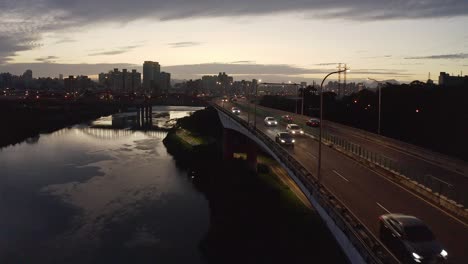 Luftdrohnenansicht,-Die-Autos-Zeigt,-Die-Während-Des-Sonnenuntergangs-Im-Hintergrund-Auf-Der-Brücke-Fahren
